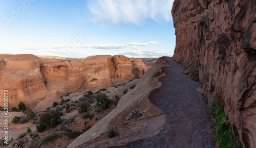 Scenic path near a dangerous cliff on a mountain during a vibrant sunny day before sunset. Taken in Arches National Park, located near Moab, Utah, United States.
