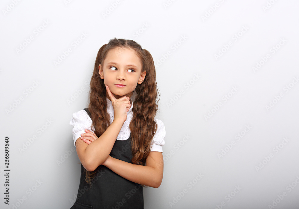 Fun pupil girl school uniform thinking and looking up on blue background with empty copy space Fun pupil girl school uniform thinking and looking up on blue background with empty copy space