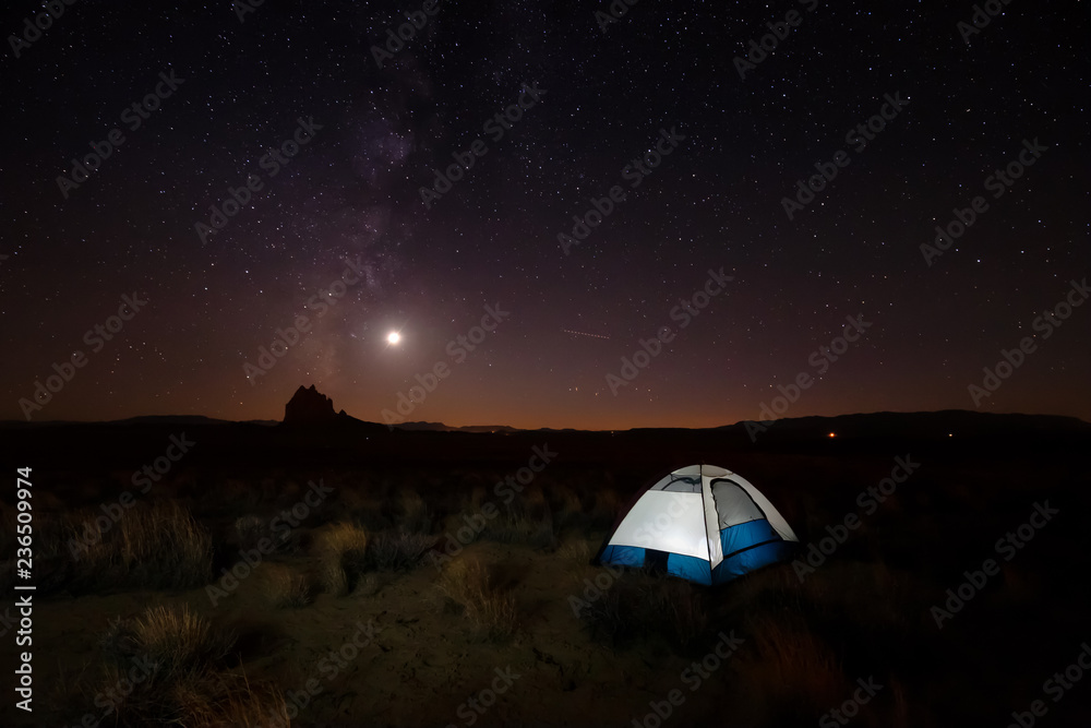 Lit tent in the desert with a mountain peak in the background during a clear night sky after sunset. Taken at Shiprock, New Mexico, United States.