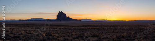 Striking panoramic landscape view of a dry desert with a mountain peak in the background during a vibrant sunset. Taken at Shiprock  New Mexico  United States.