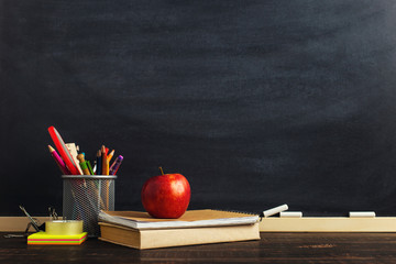 Teacher's desk with writing materials, a book and an apple, a blank for text or a background for a school theme. Copy space.