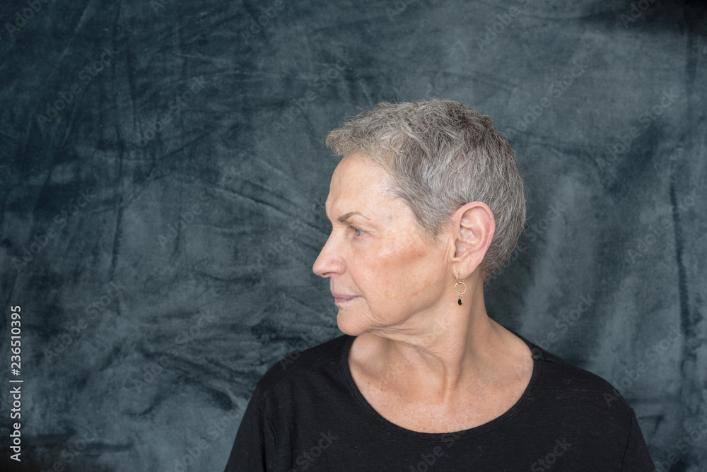 Profile view of older woman with short grey hair and black top against dark background (selective focus) Profile view of older woman with short grey hair and black top against dark background (selective focus)