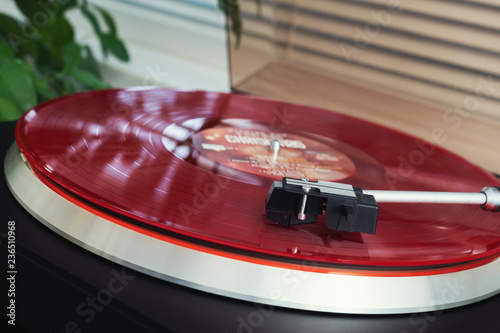 Turntable vinyl record player on a white background. Retro audio equipment for disc jockey. Sound technology for DJ to mix & play music. Red vinyl record and needle. Indoor green plant in a white pot