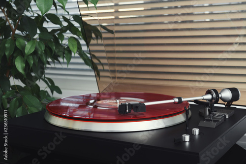 Turntable vinyl record player on a white background. Retro audio equipment for disc jockey. Sound technology for DJ to mix & play music. Red vinyl record and needle. Indoor green plant in a white pot