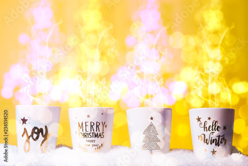 Four Christmas mugs wth christmas decoration  in  row, hot cooa and coffe dr, cozy home chrismtas, against a bokehlicious yellow background warm tone. photo