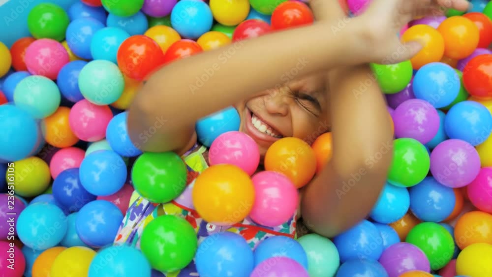 Portrait of cute African American child covered in multi coloured plastic balls in big paddling pool 