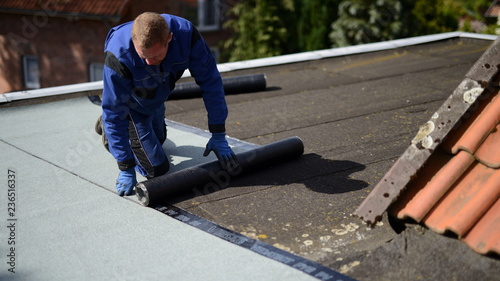 Dachdecker Facharbeiter auf Flachdach Baustelle mit Bitumen Dachpappe Baumaterial beim Abkleben vom Hallendach Haus photo