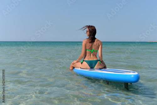 Athletic young woman sitting on a Board for SAP surfing in the sea in hot summer.