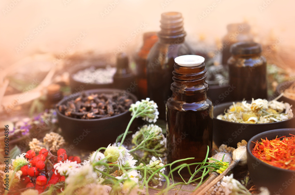 Essential oil bottles on medicinal flowers and herbs background, selective focus, toned