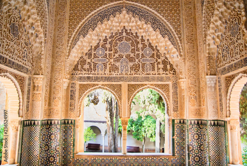 Moorish architecture in one room of the Nasrid Palaces of the Alhambra of Granada in Spain, with beautiful intricate carvings and windows overlooking a garden. photo