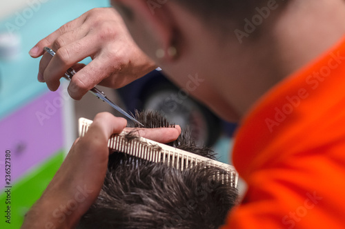 the hairdresser shears the children's haircut with scissors and comb