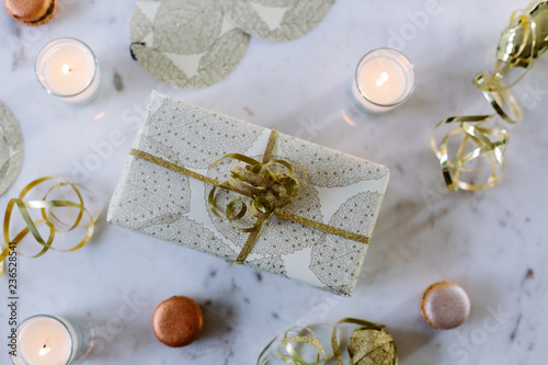 Gold theme wrapped Christmas gift with ribbon, candles and macaroons.  photo