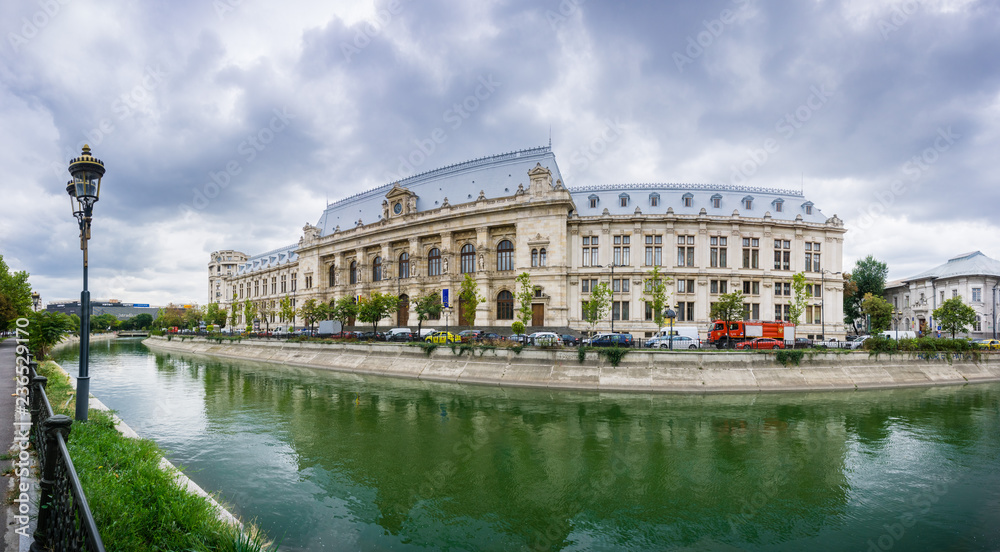 Panoramic view of Palace of Justice in downtown Bucharest reflected in Dambovita River; dramatic cloudy sky in the background, Bucharest, Romania