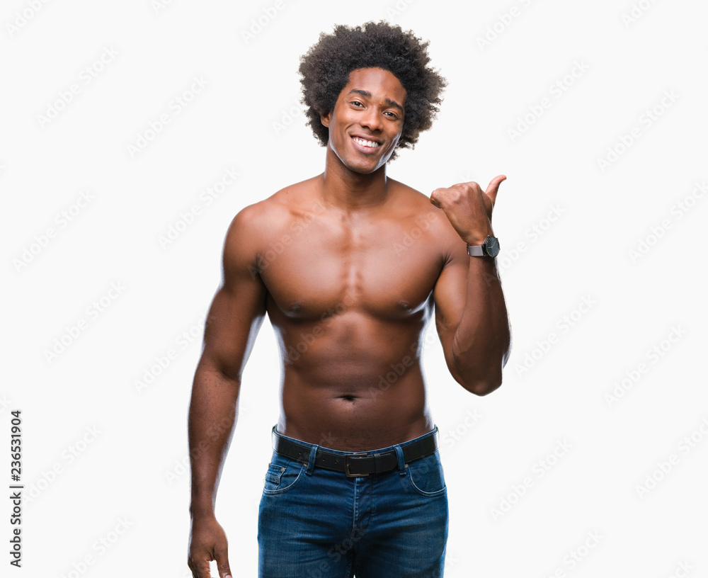 Afro american shirtless man showing nude body over isolated background smiling with happy face looking and pointing to the side with thumb up. Afro american shirtless man showing nude body over isolated background smiling with happy face looking and pointing to the side with thumb up.