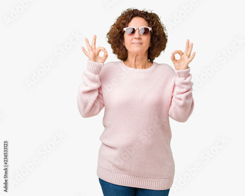 Beautiful middle ager senior woman wearing pink sweater and sunglasses over isolated background relax and smiling with eyes closed doing meditation gesture with fingers. Yoga concept.