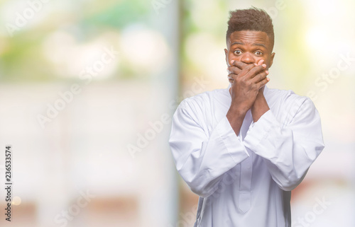 Young arabic african man wearing traditional djellaba over isolated background shocked covering mouth with hands for mistake. Secret concept.
