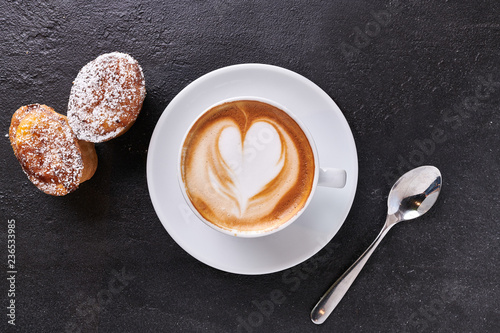 top view of cup of creamy cappuccino with the shape of a heart, on dark stone background, with sweets and icing sugar photo