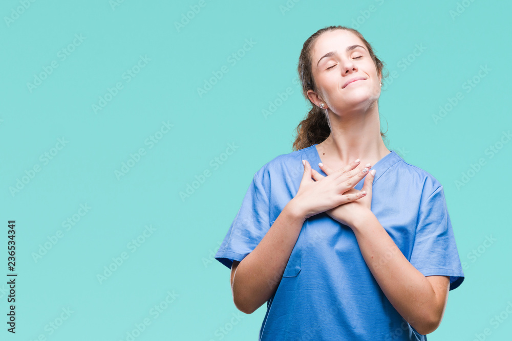 Young brunette doctor girl wearing nurse or surgeon uniform over isolated background smiling with hands on chest with closed eyes and grateful gesture on face. Health concept.