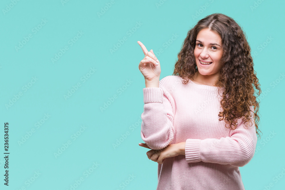 Beautiful brunette curly hair young girl wearing pink winter sweater over isolated background with a big smile on face, pointing with hand and finger to the side looking at the camera. Beautiful brunette curly hair young girl wearing pink winter sweater over isolated background with a big smile on face, pointing with hand and finger to the side looking at the camera.