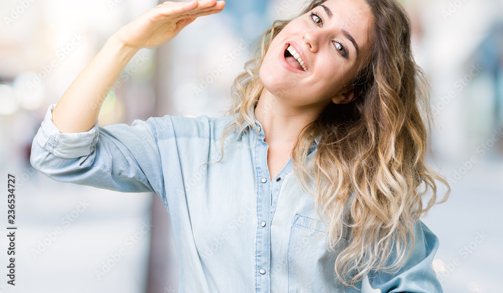 Beautiful young blonde woman over isolated background gesturing with hands showing big and large size sign, measure symbol. Smiling looking at the camera. Measuring concept. Beautiful young blonde woman over isolated background gesturing with hands showing big and large size sign, measure symbol. Smiling looking at the camera. Measuring concept.
