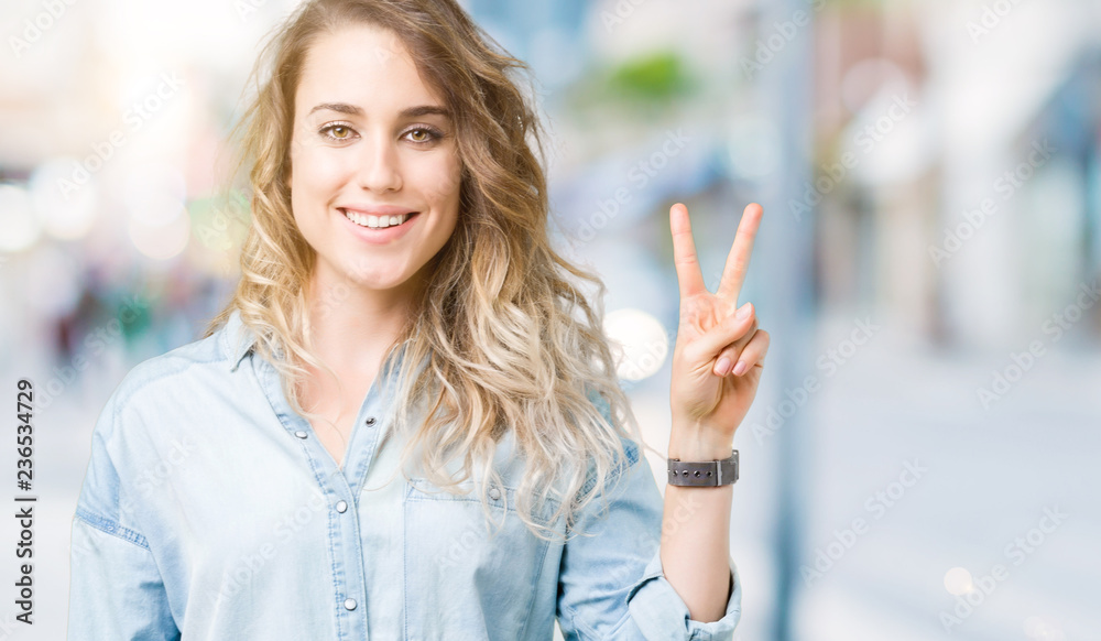 Beautiful young blonde woman over isolated background showing and pointing up with fingers number two while smiling confident and happy.