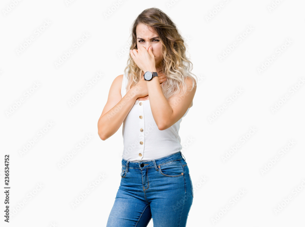 Young beautiful blonde woman over isolated background smelling something stinky and disgusting, intolerable smell, holding breath with fingers on nose. Bad smells concept. Young beautiful blonde woman over isolated background smelling something stinky and disgusting, intolerable smell, holding breath with fingers on nose. Bad smells concept.