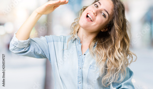 Beautiful young blonde woman over isolated background gesturing with hands showing big and large size sign, measure symbol. Smiling looking at the camera. Measuring concept.