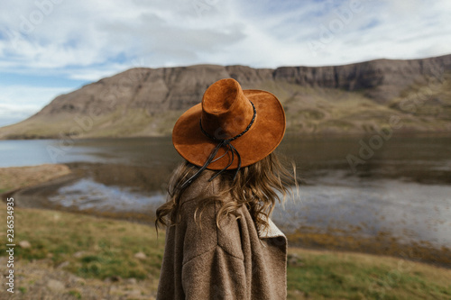 A portrait of a girl wearing beige poncho and a brown hat surrounded by icelandic majestic landscapes 