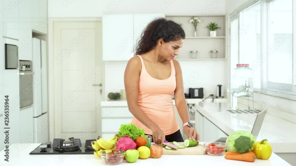 Attractive young woman making vegetable and fruit salad while looking recipe on the laptop in the kitchen. Shot in 4k resolution Attractive young woman making vegetable and fruit salad while looking recipe on the laptop in the kitchen. Shot in 4k resolution