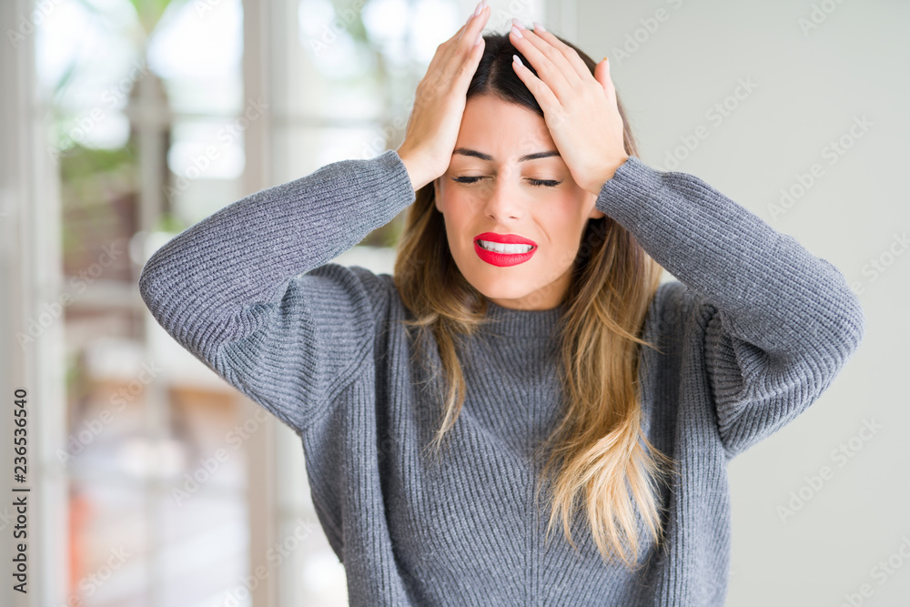 Young beautiful woman wearing winter sweater at home suffering from headache desperate and stressed because pain and migraine. Hands on head. Young beautiful woman wearing winter sweater at home suffering from headache desperate and stressed because pain and migraine. Hands on head.