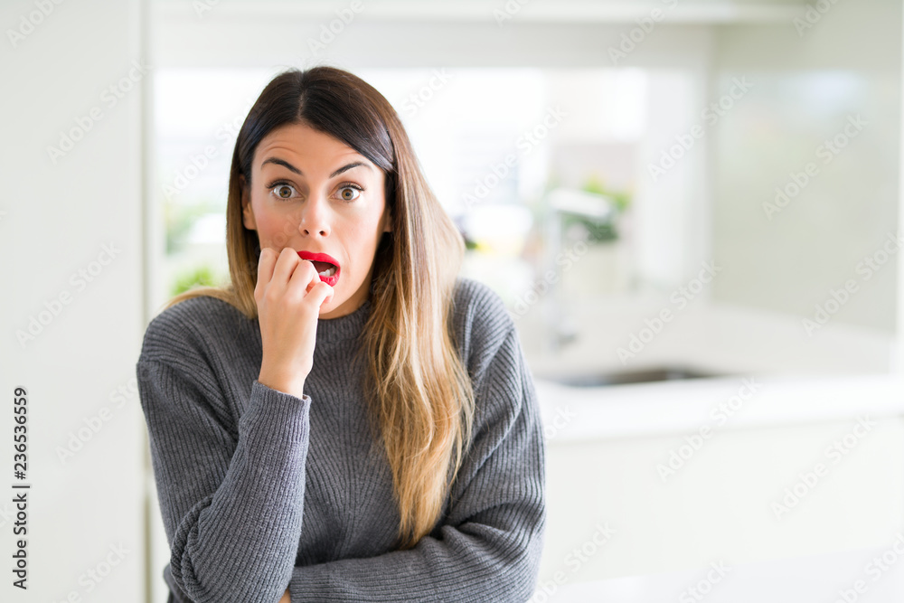 Young beautiful woman wearing winter sweater at home looking stressed and nervous with hands on mouth biting nails. Anxiety problem. Young beautiful woman wearing winter sweater at home looking stressed and nervous with hands on mouth biting nails. Anxiety problem.