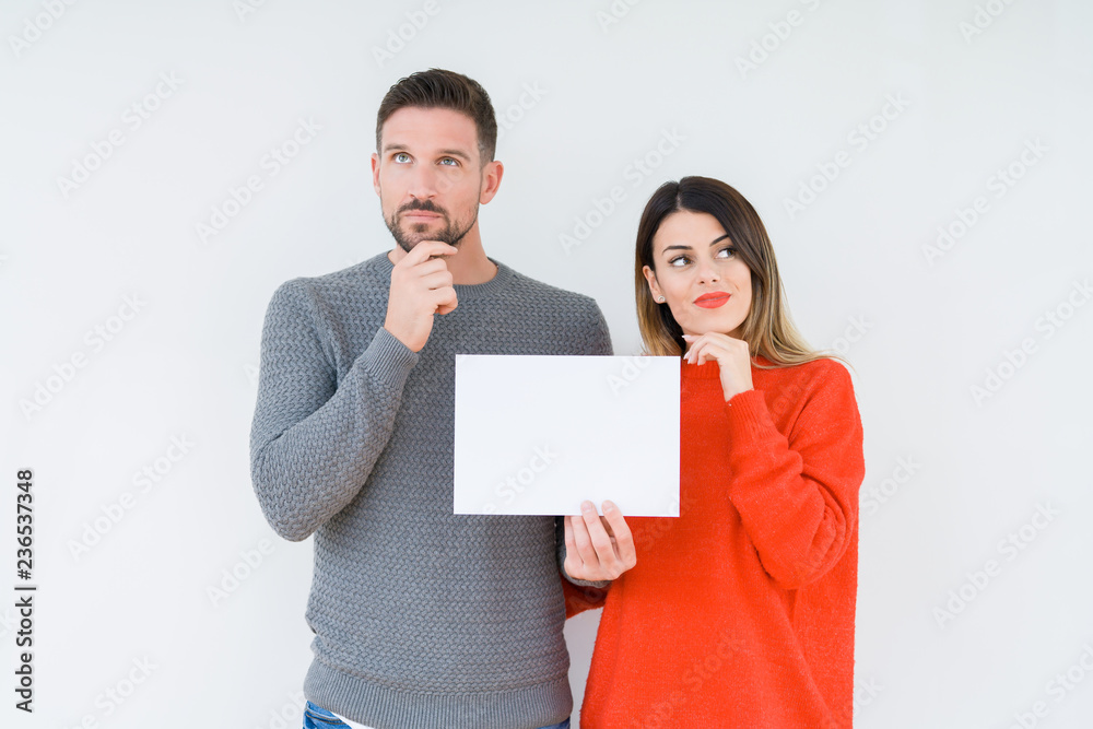 Young couple holding blank sheet paper over isolated background serious face thinking about question, very confused idea Young couple holding blank sheet paper over isolated background serious face thinking about question, very confused idea