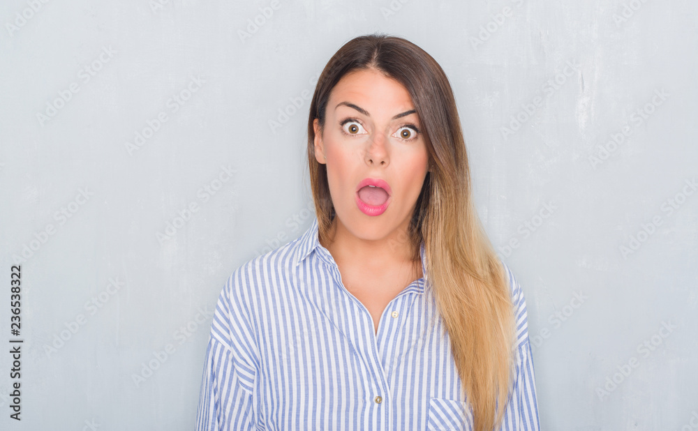Young adult woman over grunge grey wall wearing business shirt afraid and shocked with surprise expression, fear and excited face. Young adult woman over grunge grey wall wearing business shirt afraid and shocked with surprise expression, fear and excited face.