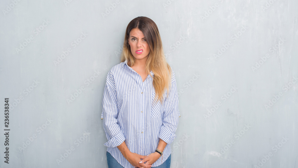 Young adult woman over grey grunge wall wearing fashion business outfit skeptic and nervous, frowning upset because of problem. Negative person. Young adult woman over grey grunge wall wearing fashion business outfit skeptic and nervous, frowning upset because of problem. Negative person.