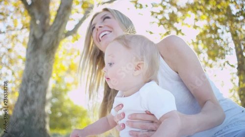 Portrait of attractive blonde Caucasian mom and her young baby boy enjoying togetherness outdoors in the park 
