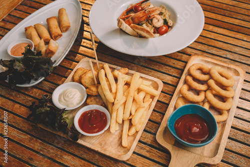 onion rings, french fries, chicken nuggets, Spring rolls, spaghetti pasta with shrimps over wooden table