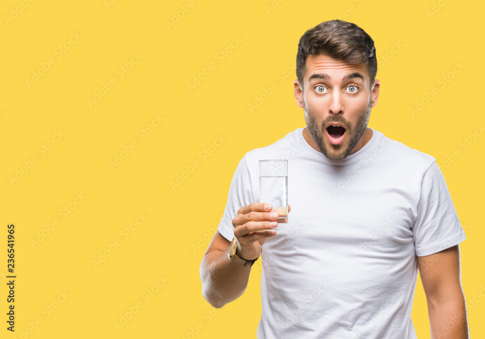 Young handsome man drinking glass of water over isolated background scared in shock with a surprise face, afraid and excited with fear expression