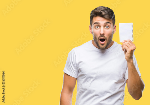 Young handsome man holding notebook over isolated background scared in shock with a surprise face, afraid and excited with fear expression