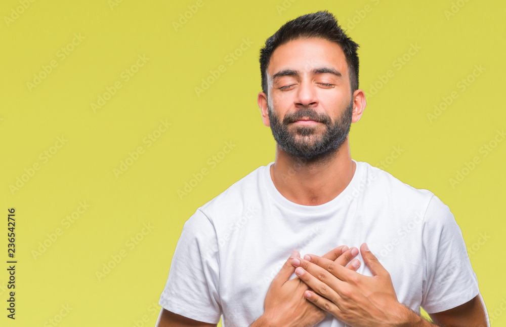 Adult hispanic man over isolated background smiling with hands on chest with closed eyes and grateful gesture on face. Health concept. Adult hispanic man over isolated background smiling with hands on chest with closed eyes and grateful gesture on face. Health concept.