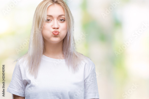 Young blonde woman over isolated background puffing cheeks with funny face. Mouth inflated with air, crazy expression.