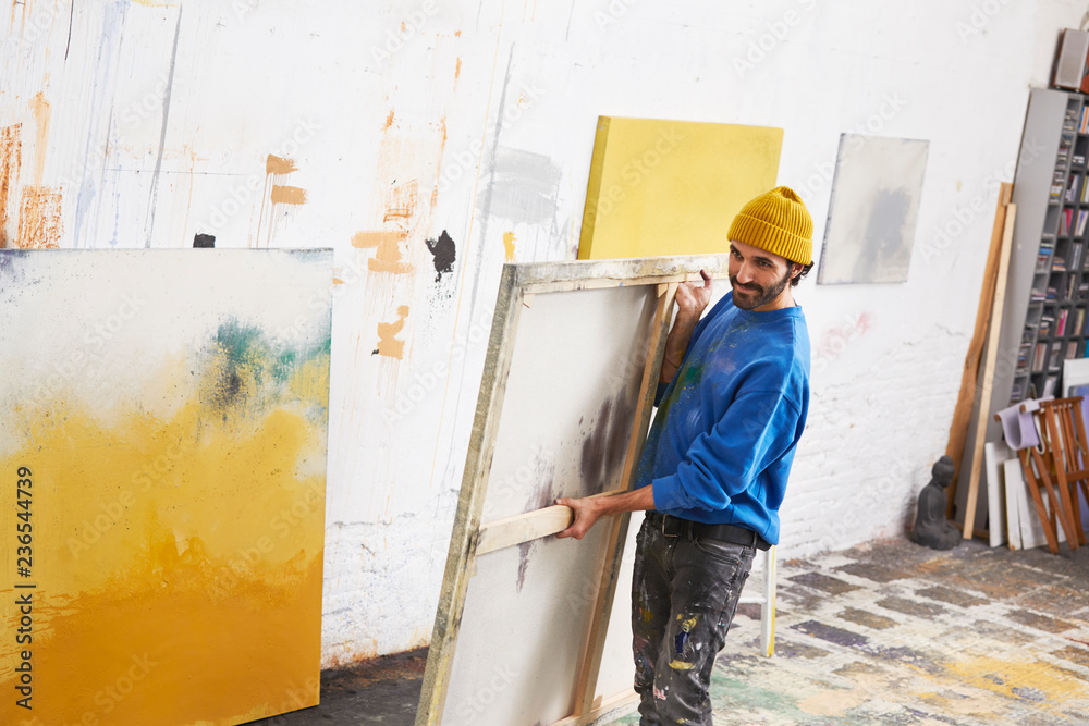 Male Painter Carrying Painting In Studio Male Painter Carrying Painting In Studio