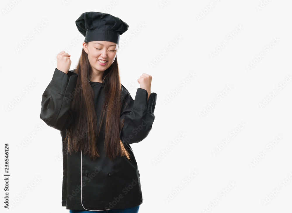 Young Chinese woman over isolated background wearing chef uniform very happy and excited doing winner gesture with arms raised, smiling and screaming for success. Celebration concept. Young Chinese woman over isolated background wearing chef uniform very happy and excited doing winner gesture with arms raised, smiling and screaming for success. Celebration concept.