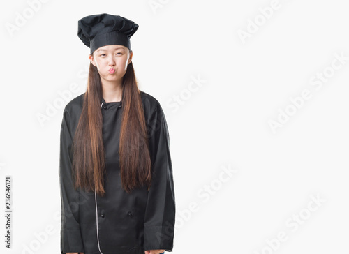 Young Chinese woman over isolated background wearing chef uniform puffing cheeks with funny face. Mouth inflated with air, crazy expression.