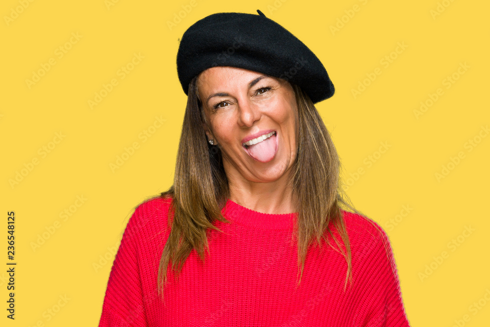 Middle age adult woman wearing fashion beret over isolated background sticking tongue out happy with funny expression. Emotion concept. Middle age adult woman wearing fashion beret over isolated background sticking tongue out happy with funny expression. Emotion concept.