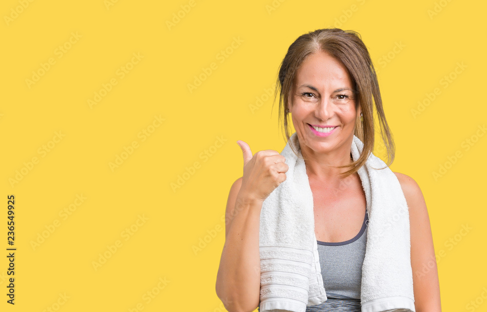 Beautiful middle age woman wearing sport clothes and a towel over isolated background doing happy thumbs up gesture with hand. Approving expression looking at the camera with showing success. Beautiful middle age woman wearing sport clothes and a towel over isolated background doing happy thumbs up gesture with hand. Approving expression looking at the camera with showing success.