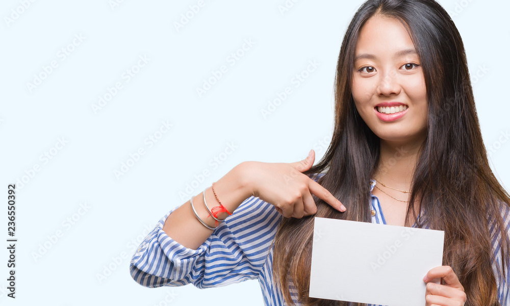 Young asian woman holding blank card over isolated background with surprise face pointing finger to himself Young asian woman holding blank card over isolated background with surprise face pointing finger to himself