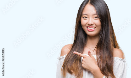 Young asian woman over isolated background cheerful with a smile of face pointing with hand and finger up to the side with happy and natural expression on face looking at the camera.
