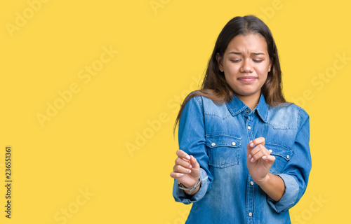 Young beautiful brunette woman wearing blue denim shirt over isolated background disgusted expression, displeased and fearful doing disgust face because aversion reaction. With hands raised