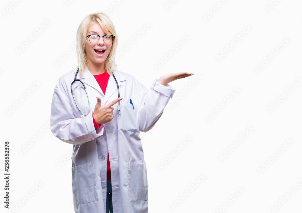 Young beautiful blonde doctor woman wearing medical uniform over isolated background amazed and smiling to the camera while presenting with hand and pointing with finger. Young beautiful blonde doctor woman wearing medical uniform over isolated background amazed and smiling to the camera while presenting with hand and pointing with finger.
