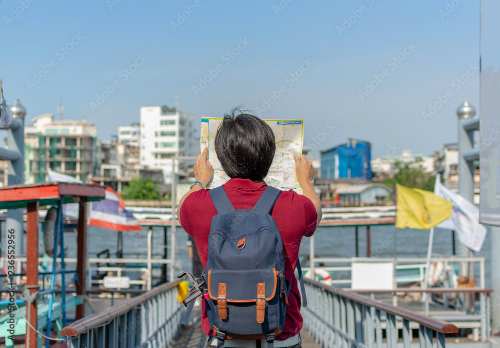 Backpack asian young man as a tourist looking at the map travelling along Chaopraya riverside , Bangkok.
